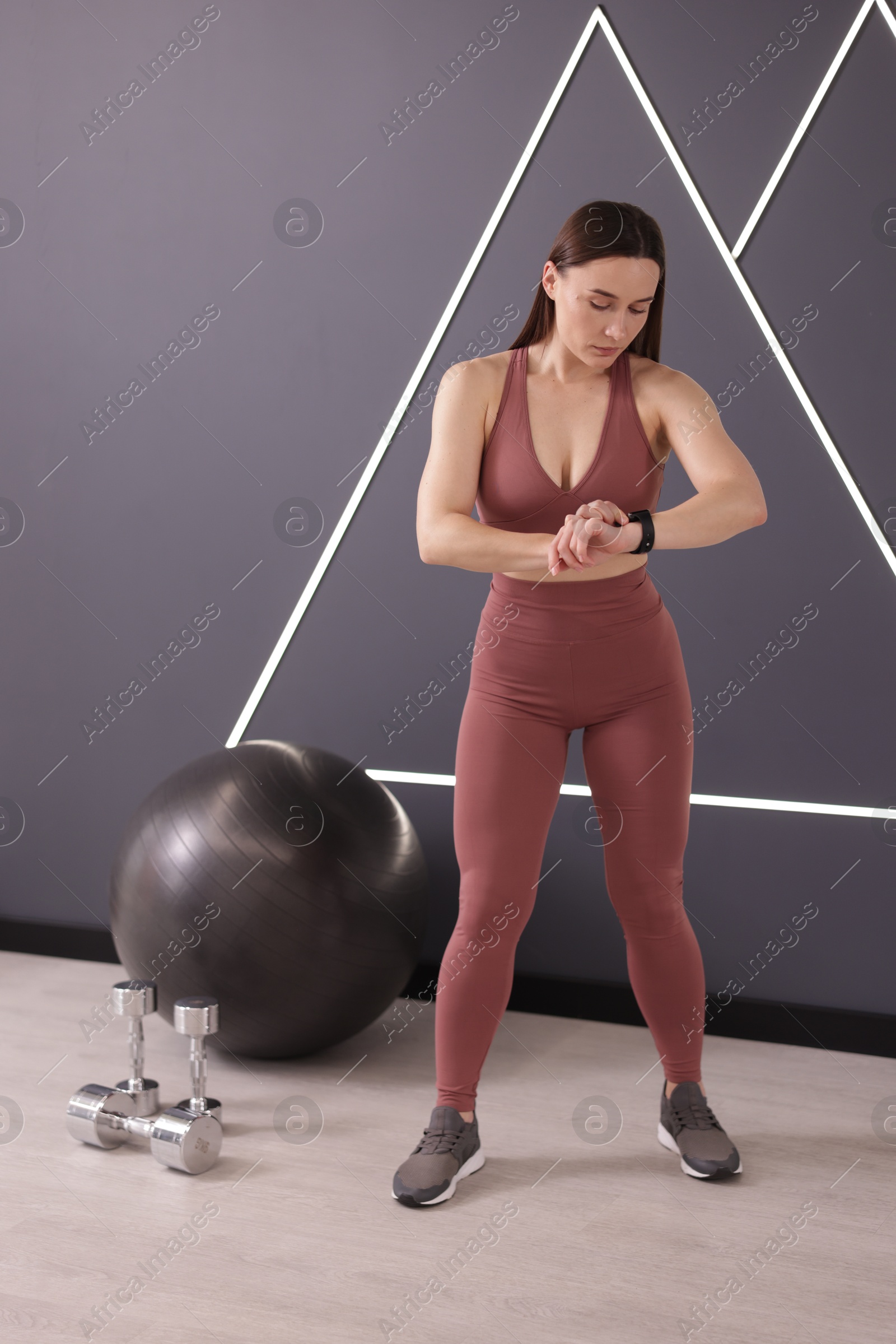 Photo of Beautiful woman checking fitness tracker during training in studio