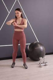 Photo of Beautiful woman checking fitness tracker during training in studio