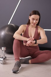 Photo of Beautiful woman checking fitness tracker during training in studio