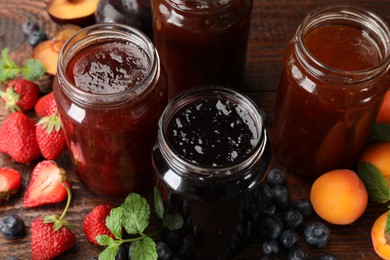 Photo of Different jams in jars and ingredients on wooden table, closeup