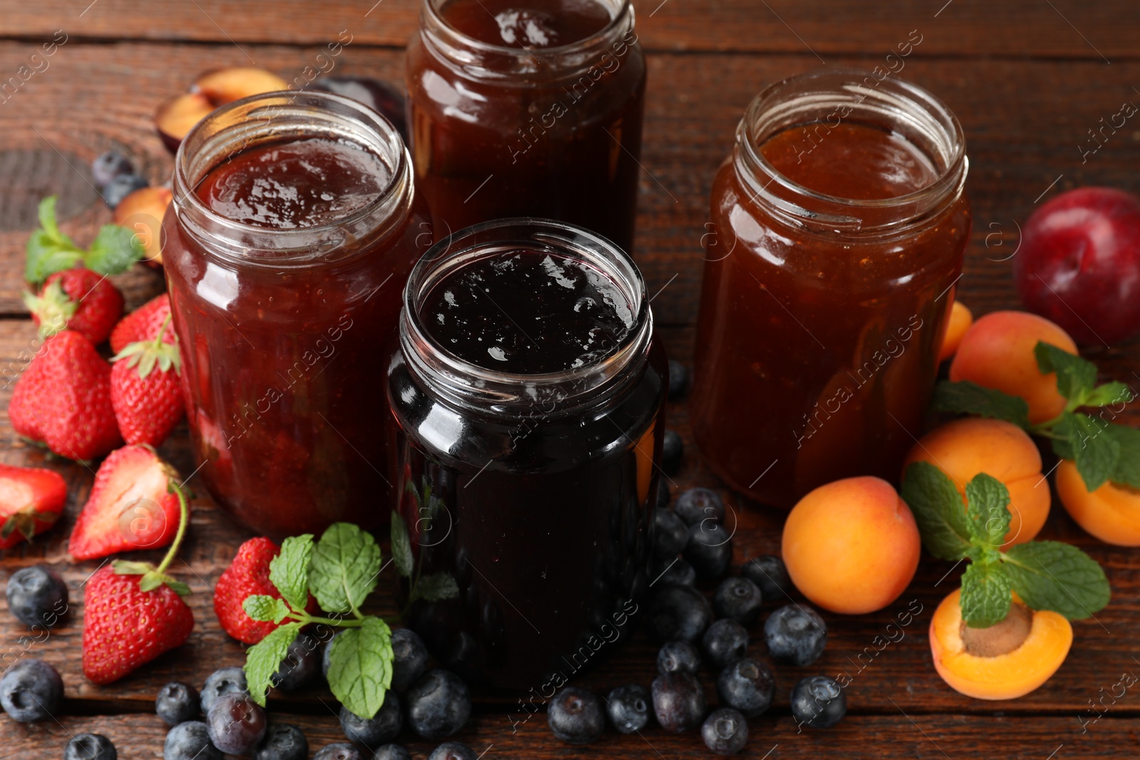Different jams in jars and ingredients on wooden table, closeup Photo of Different jams in jars and ingredients on wooden table, closeup