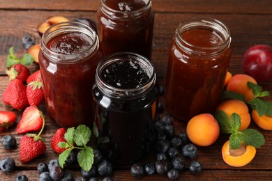 Photo of Different jams in jars and ingredients on wooden table, closeup