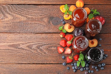 Photo of Different jams in jars and ingredients on wooden table, flat lay. Space for text