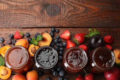 Photo of Different jams in jars and ingredients on wooden table, flat lay. Space for text