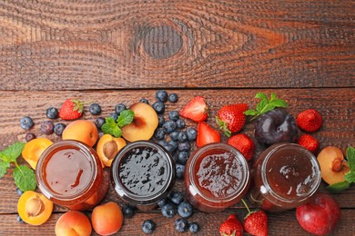 Photo of Different jams in jars and ingredients on wooden table, flat lay. Space for text