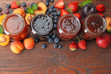 Photo of Different jams in jars and ingredients on wooden table, flat lay. Space for text