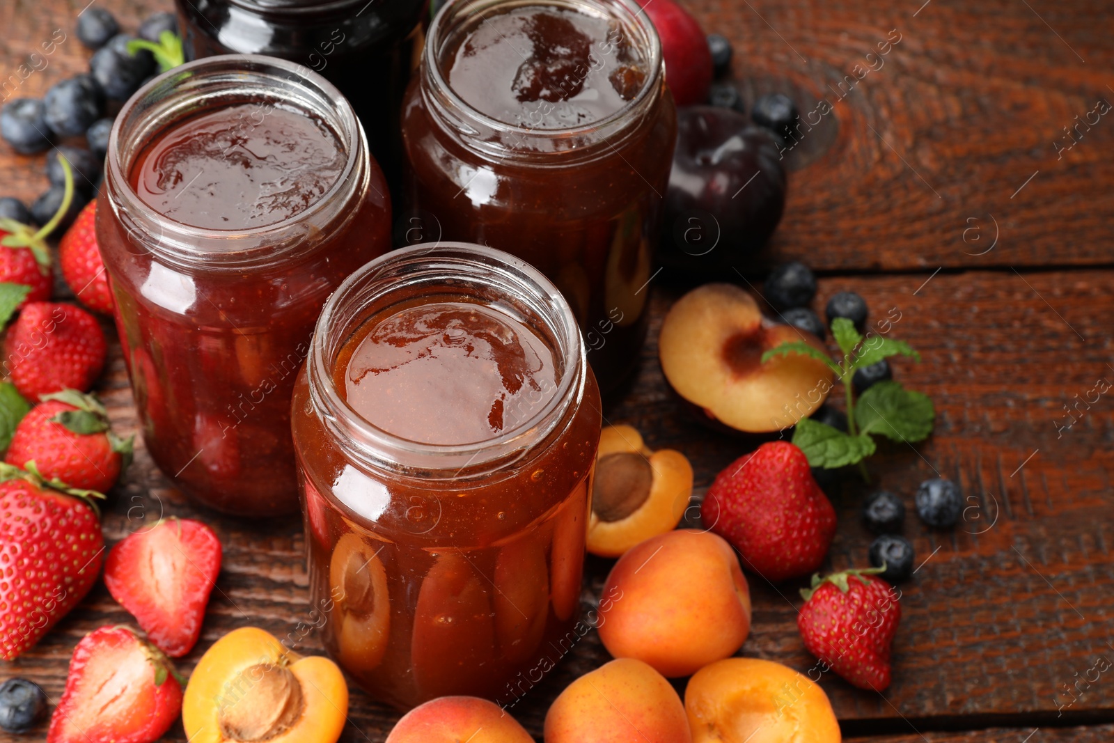 Different jams in jars and ingredients on wooden table, closeup Photo of Different jams in jars and ingredients on wooden table, closeup