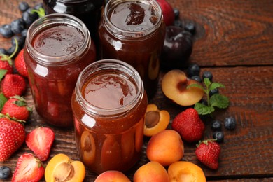 Photo of Different jams in jars and ingredients on wooden table, closeup