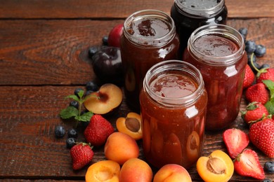 Photo of Different jams in jars and ingredients on wooden table, closeup