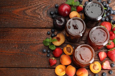 Photo of Different jams in jars and ingredients on wooden table, flat lay. Space for text