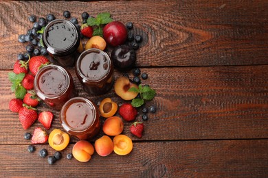 Photo of Different jams in jars and ingredients on wooden table, flat lay. Space for text