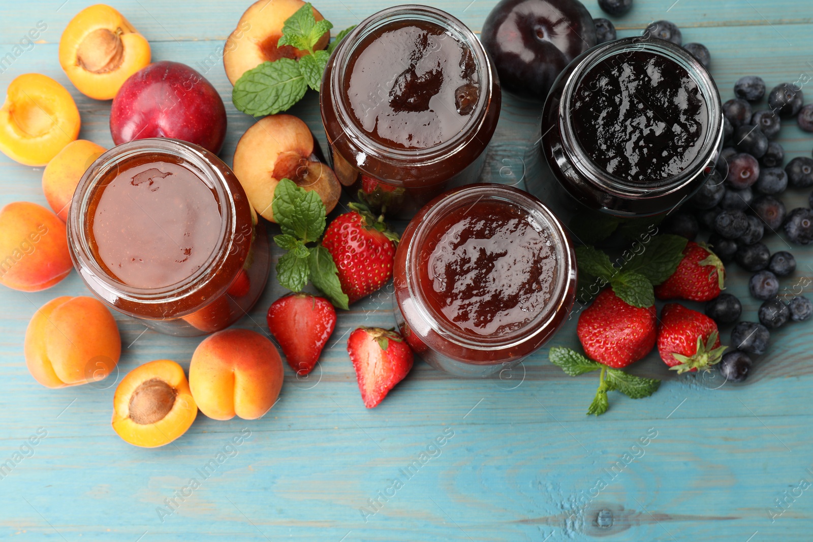 Different jams in jars and ingredients on blue wooden table, flat lay Photo of Different jams in jars and ingredients on blue wooden table, flat lay