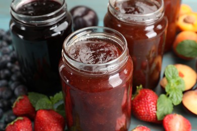 Photo of Different jams in jars and ingredients on blue wooden table, closeup