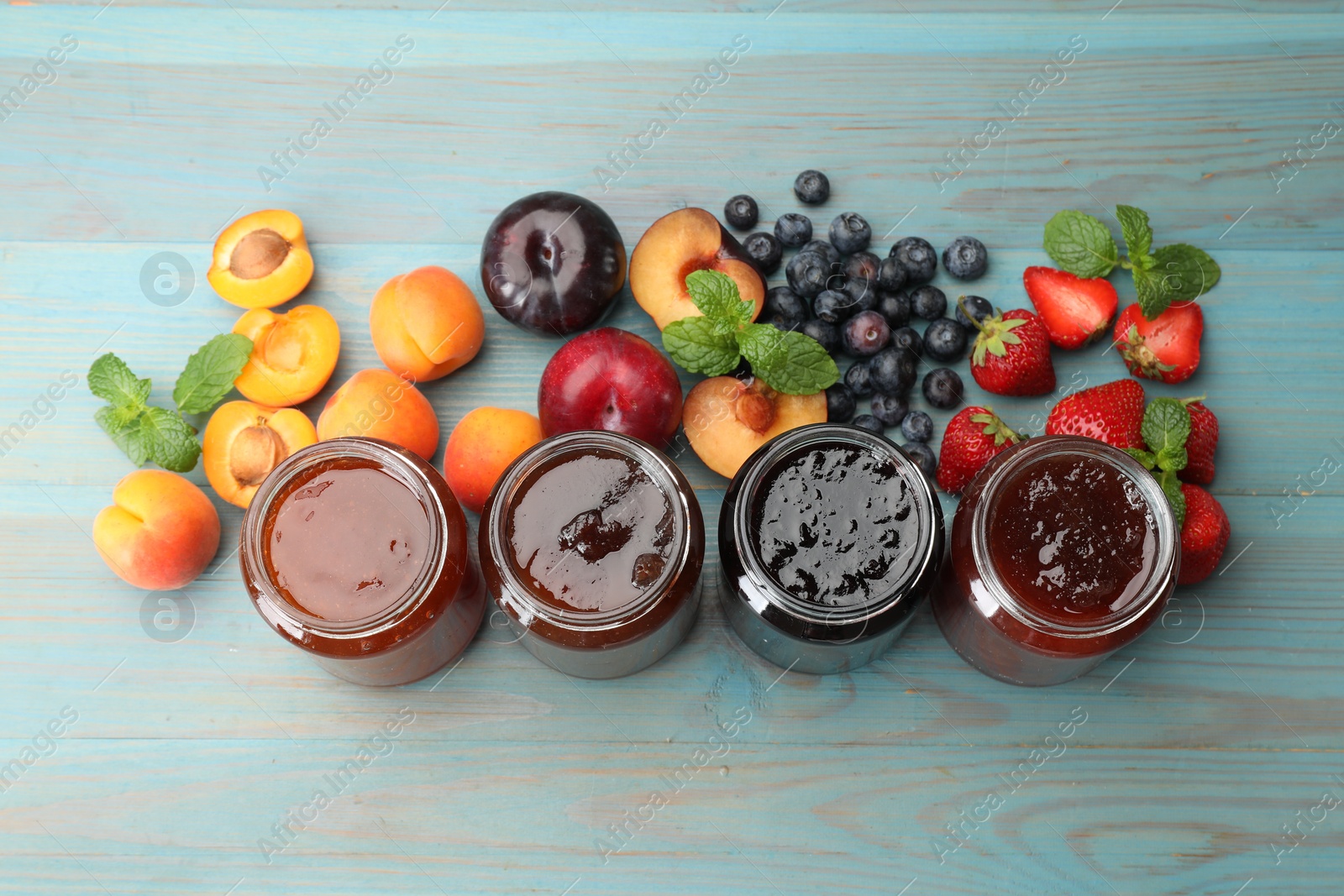 Different jams in jars and ingredients on blue wooden table, flat lay Photo of Different jams in jars and ingredients on blue wooden table, flat lay