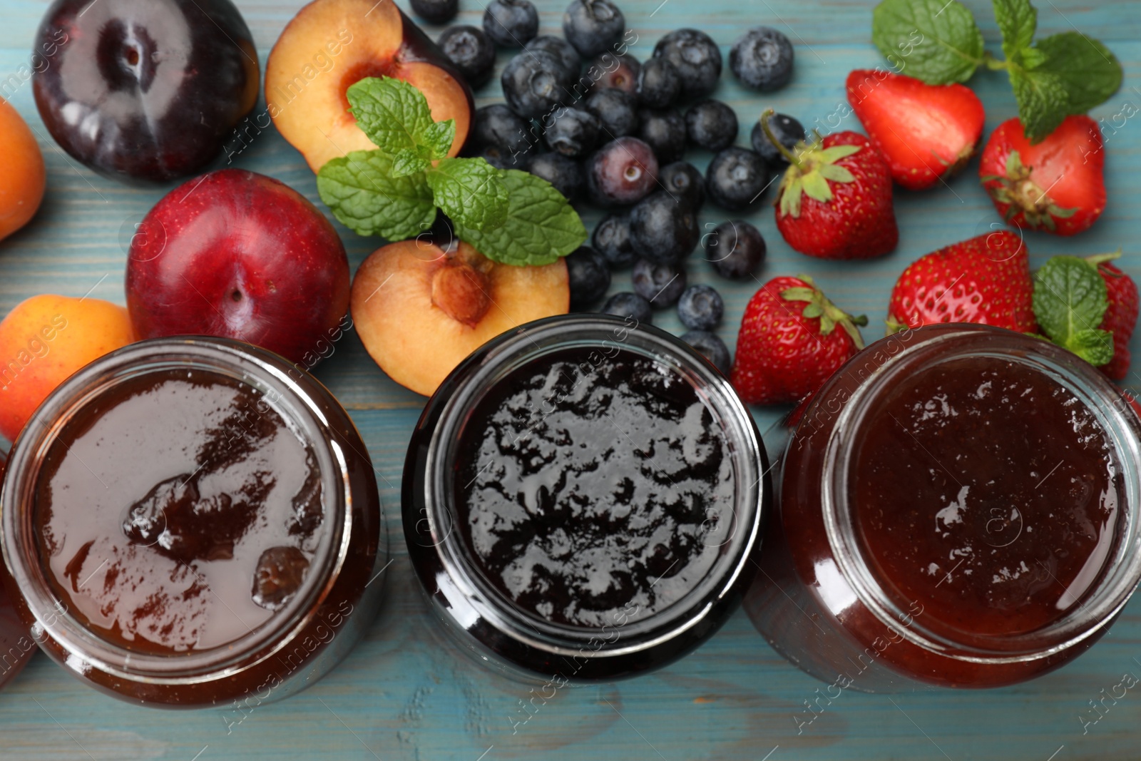 Different jams in jars and ingredients on blue wooden table, flat lay Photo of Different jams in jars and ingredients on blue wooden table, flat lay