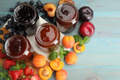 Photo of Different jams in jars and ingredients on blue wooden table, flat lay. Space for text