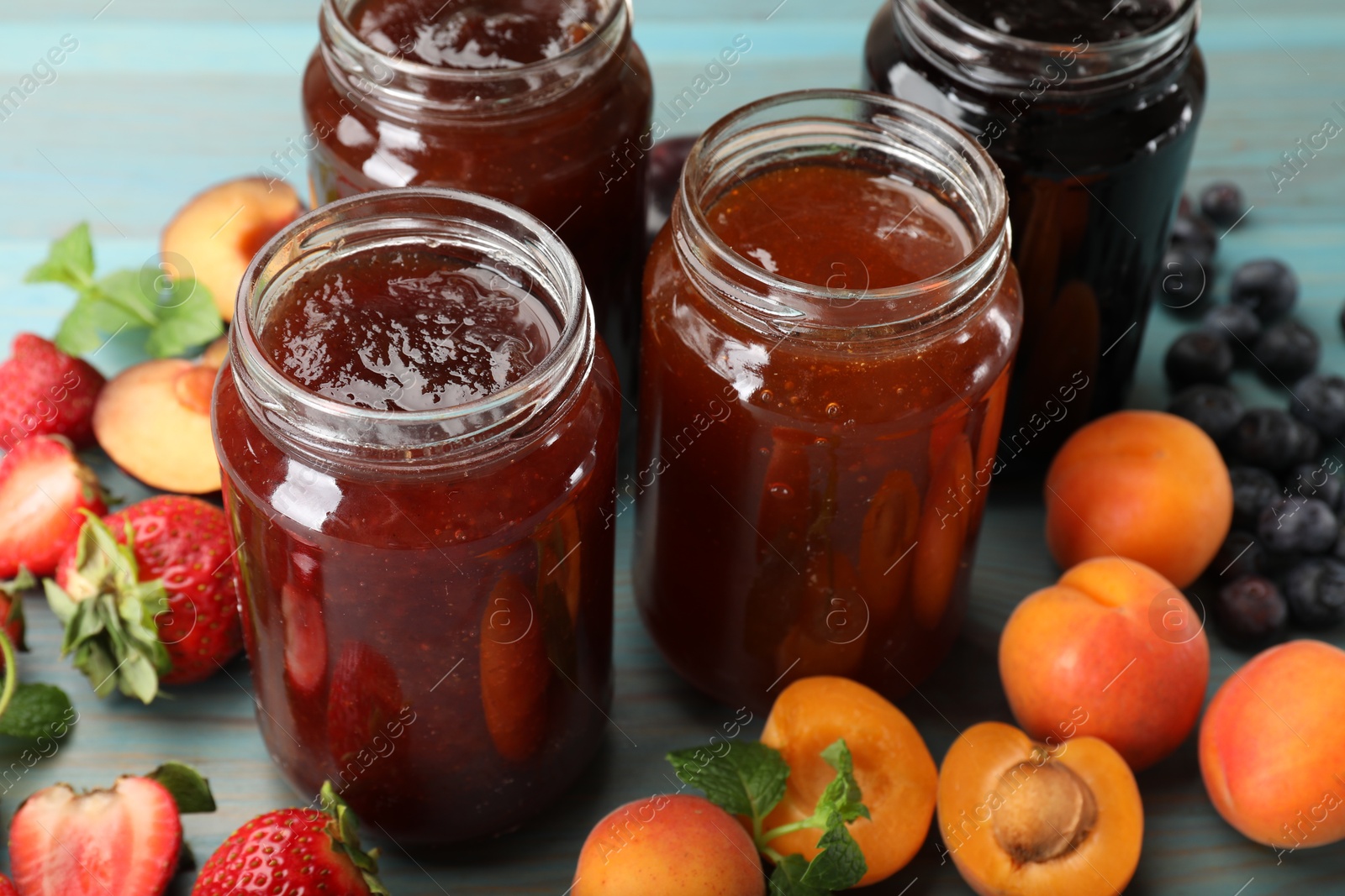 Different jams in jars and ingredients on blue wooden table, closeup Photo of Different jams in jars and ingredients on blue wooden table, closeup