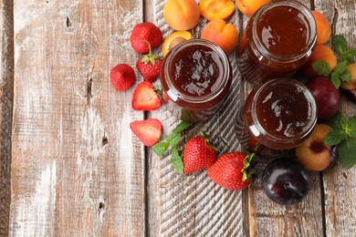 Photo of Different jams in jars and ingredients on wooden table, flat lay. Space for text