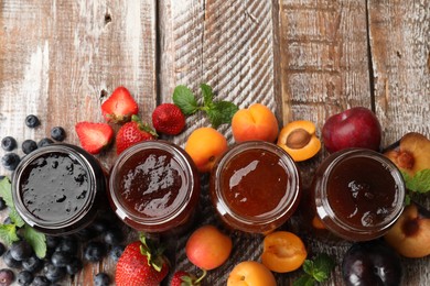 Photo of Different jams in jars and ingredients on wooden table, flat lay. Space for text