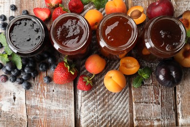 Photo of Different jams in jars and ingredients on wooden table, flat lay. Space for text