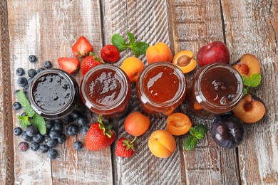 Photo of Different jams in jars and ingredients on wooden table, flat lay