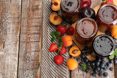 Photo of Different jams in jars and ingredients on wooden table, flat lay. Space for text