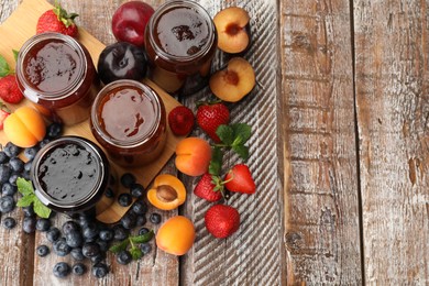 Photo of Different jams in jars and ingredients on wooden table, flat lay. Space for text