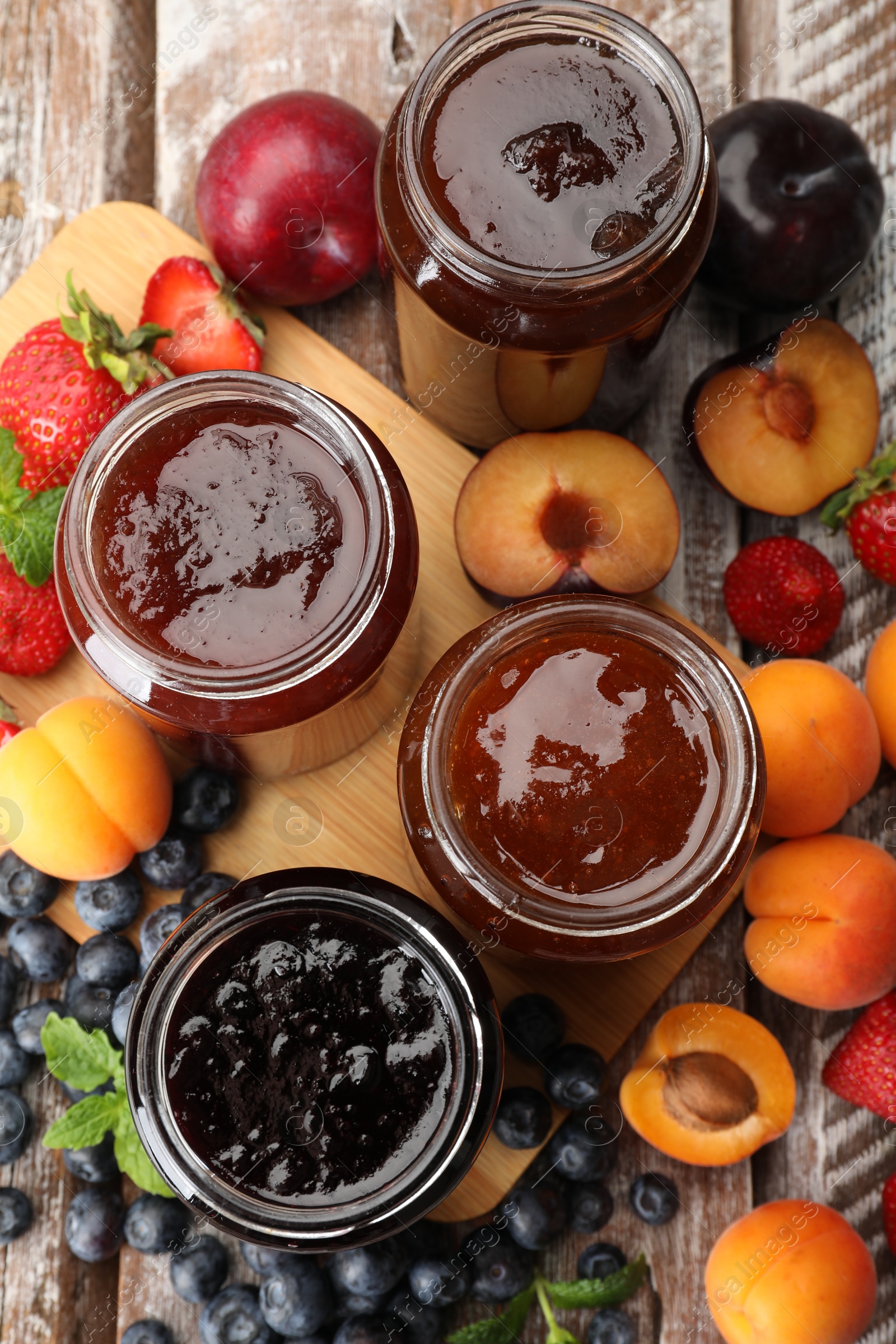 Different jams in jars and ingredients on wooden table, flat lay Photo of Different jams in jars and ingredients on wooden table, flat lay
