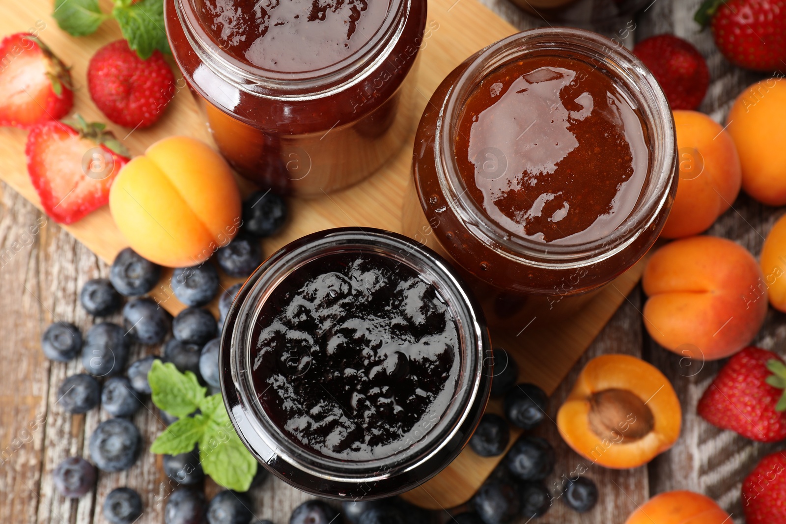 Different jams in jars and ingredients on wooden table, flat lay Photo of Different jams in jars and ingredients on wooden table, flat lay