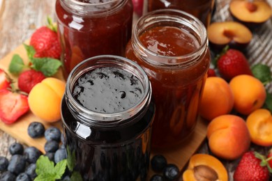 Photo of Different jams in jars and ingredients on wooden table, closeup