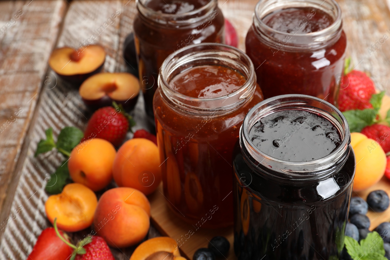 Different jams in jars and ingredients on wooden table, closeup Photo of Different jams in jars and ingredients on wooden table, closeup