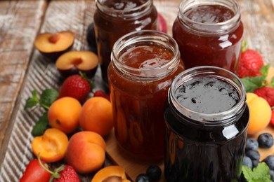 Photo of Different jams in jars and ingredients on wooden table, closeup