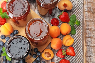 Photo of Different jams in jars and ingredients on wooden table, flat lay