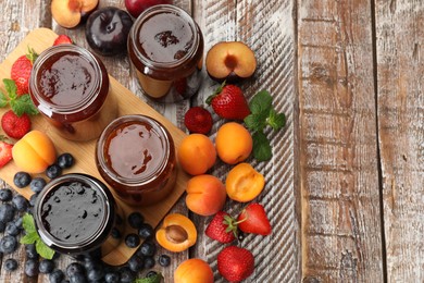 Photo of Different jams in jars and ingredients on wooden table, flat lay. Space for text