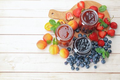 Photo of Different jams in jars and ingredients on white wooden table, flat lay. Space for text