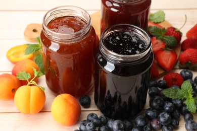 Photo of Different jams in jars and ingredients on white wooden table, closeup