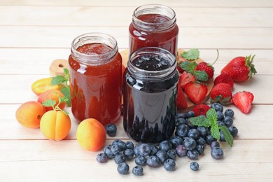 Photo of Different jams in jars and ingredients on white wooden table