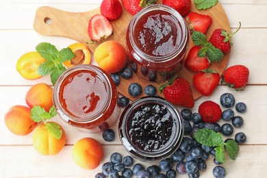 Photo of Different jams in jars and ingredients on white wooden table, flat lay