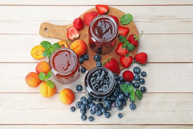 Photo of Different jams in jars and ingredients on white wooden table, flat lay