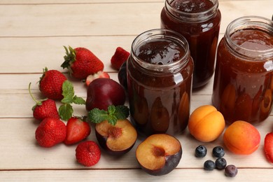Photo of Different jams in jars and ingredients on white wooden table