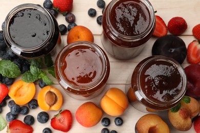 Photo of Different jams in jars and ingredients on white wooden table, flat lay