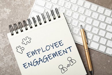 Image of Employee engagement. Words and drawings in notebook, pen and computer keyboard on grey table, top view