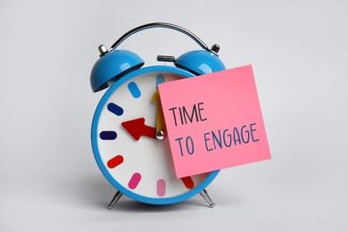 Image of Time to engage. Alarm clock with sticky note on white background