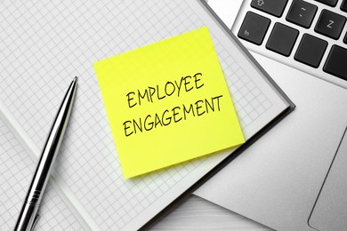 Image of Employee engagement. Notebook with pen. yellow paper note and laptop on table, top view