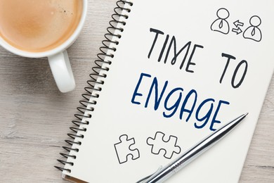 Image of Time to engage. Words and drawings in notebook and coffee on wooden table, top view