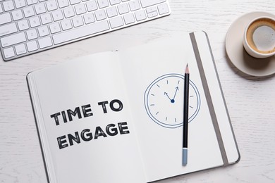 Image of Time to engage. Words and drawing in notebook, pencil, coffee and computer keyboard on white wooden table, top view