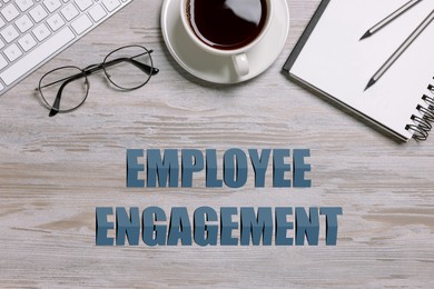Image of Employee engagement. Office workplace with coffee, stationery and computer keyboard on wooden table. top view