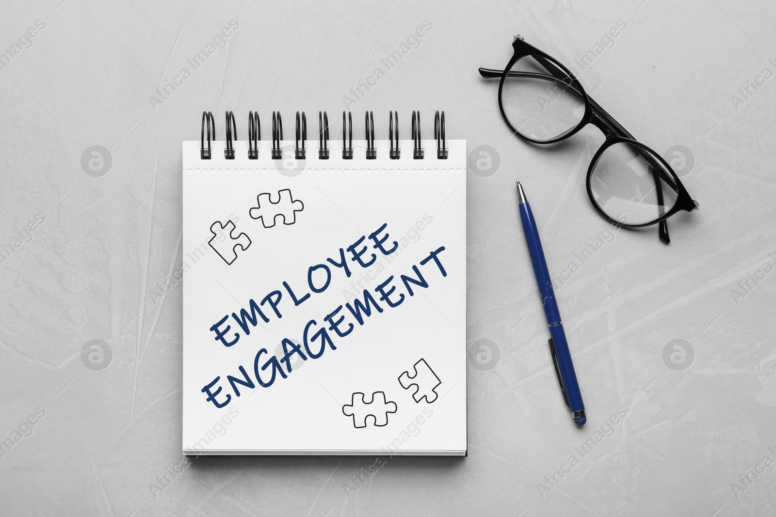 Image of Employee engagement. Words and drawings in notebook, pen and eyeglasses on grey table, top view