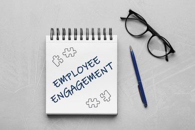 Image of Employee engagement. Words and drawings in notebook, pen and eyeglasses on grey table, top view