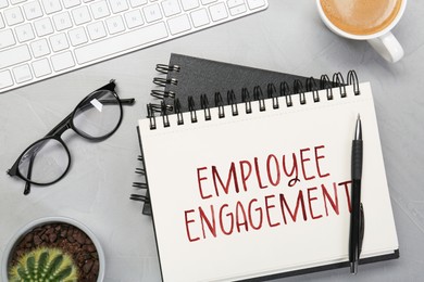 Image of Employee engagement. Words in notebook, pen, coffee and computer keyboard on grey table, top view